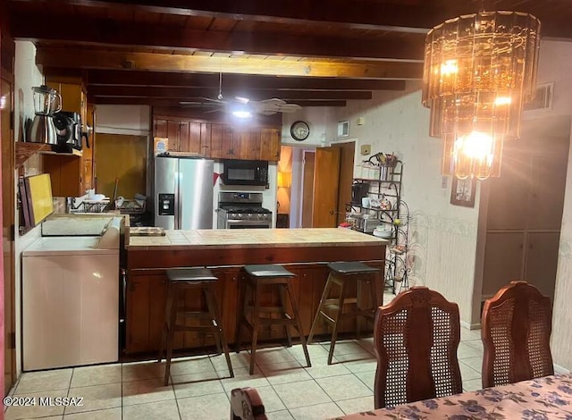 kitchen with beamed ceiling, hanging light fixtures, stainless steel appliances, and light tile patterned floors