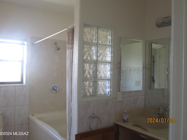 bathroom featuring tiled shower / bath combo, vanity, and tile walls