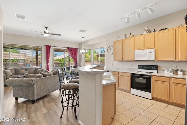 kitchen featuring sink, a breakfast bar area, decorative light fixtures, light brown cabinets, and electric range