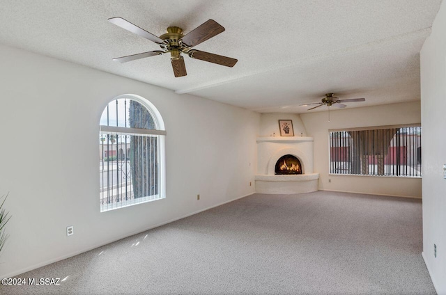 unfurnished living room featuring a ceiling fan, a warm lit fireplace, carpet flooring, and a textured ceiling