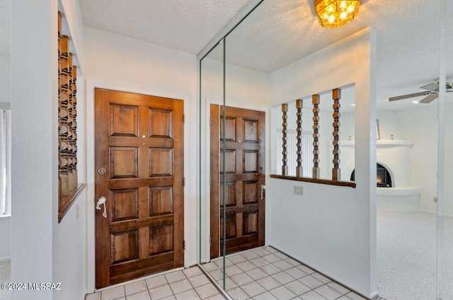 foyer entrance with ceiling fan, light colored carpet, a brick fireplace, and a textured ceiling