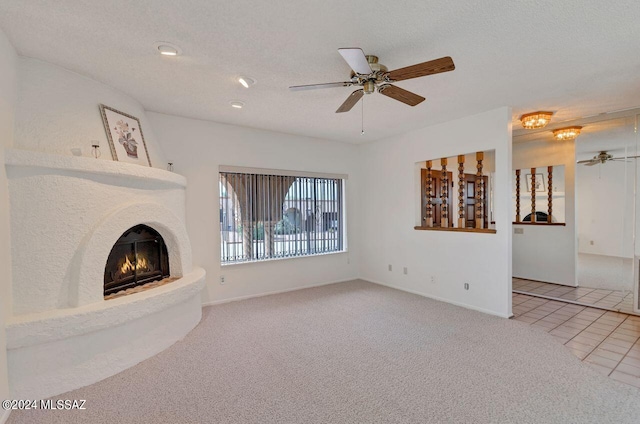 unfurnished living room featuring a warm lit fireplace, ceiling fan, carpet, tile patterned flooring, and a textured ceiling