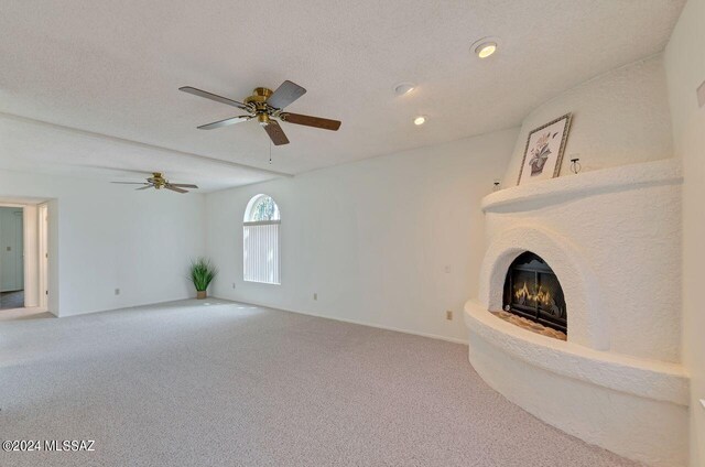 unfurnished living room with a fireplace, carpet floors, ceiling fan, and a textured ceiling