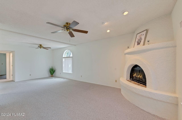 unfurnished living room featuring a ceiling fan, carpet flooring, a fireplace, and a textured ceiling