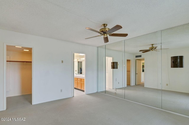 unfurnished bedroom with light carpet, a closet, a spacious closet, and a textured ceiling