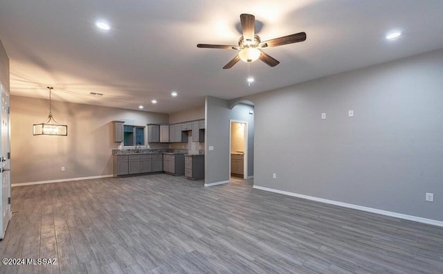 unfurnished living room with ceiling fan with notable chandelier and dark wood-type flooring