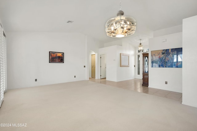 spare room featuring arched walkways, light colored carpet, an inviting chandelier, light tile patterned flooring, and vaulted ceiling