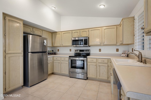 kitchen with lofted ceiling, stainless steel appliances, light countertops, light brown cabinetry, and a sink