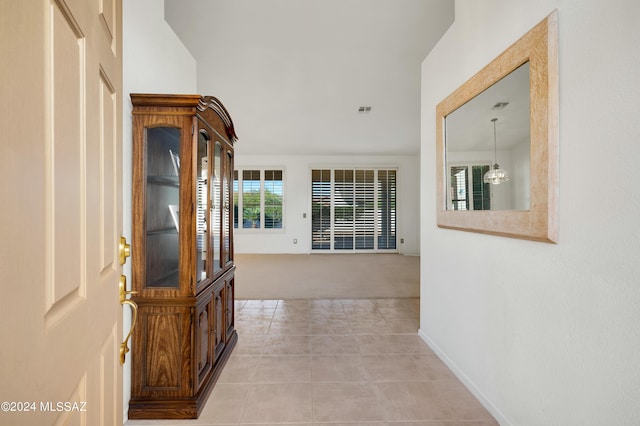 corridor featuring light carpet, light tile patterned floors, baseboards, and visible vents