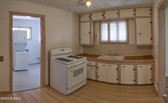 kitchen featuring stacked washer / dryer, tasteful backsplash, sink, white range with gas stovetop, and light hardwood / wood-style floors