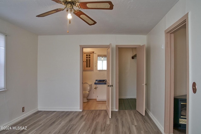 unfurnished bedroom with ceiling fan, heating unit, ensuite bathroom, and light hardwood / wood-style floors