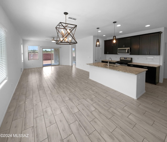 kitchen featuring a kitchen island with sink, light wood-type flooring, stainless steel appliances, sink, and decorative light fixtures