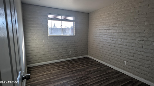 empty room featuring dark wood-type flooring and brick wall