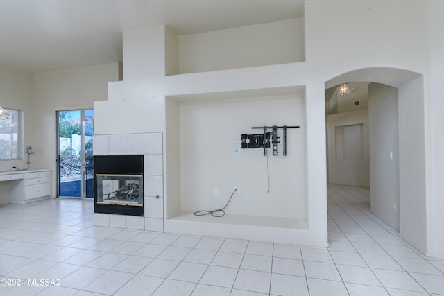 unfurnished living room with light tile patterned floors, a towering ceiling, and a tiled fireplace