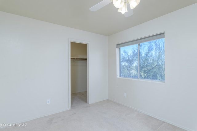 unfurnished bedroom featuring ceiling fan, a spacious closet, light carpet, and a closet