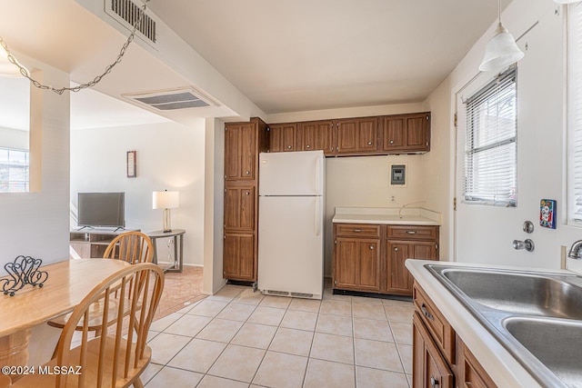 kitchen with white refrigerator, decorative light fixtures, sink, and light tile patterned floors