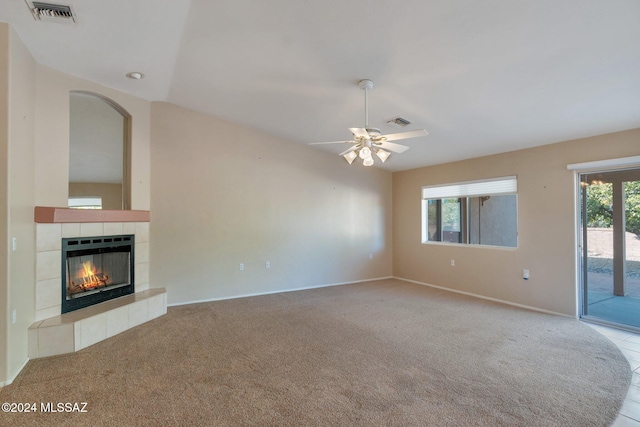 unfurnished living room with a tiled fireplace, light carpet, and ceiling fan