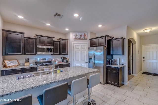 kitchen featuring appliances with stainless steel finishes, light stone counters, light tile patterned floors, sink, and dark brown cabinetry