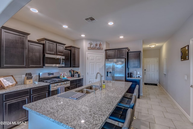 kitchen featuring light stone counters, light tile patterned flooring, an island with sink, stainless steel appliances, and sink