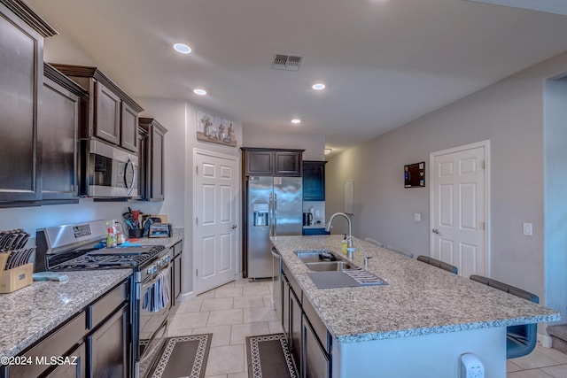 kitchen featuring a kitchen island with sink, light stone countertops, light tile patterned floors, stainless steel appliances, and sink