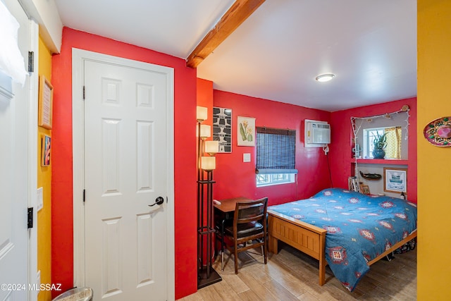 bedroom featuring a wall mounted air conditioner, hardwood / wood-style floors, and beamed ceiling