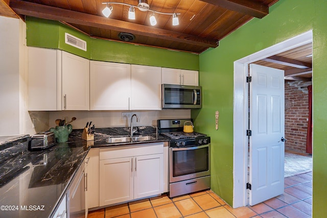 kitchen featuring stainless steel appliances, brick wall, beam ceiling, sink, and white cabinetry