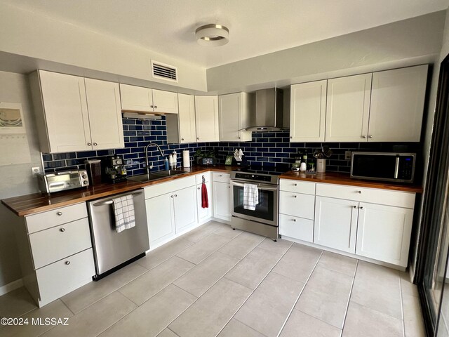 kitchen with wooden counters, wall chimney range hood, backsplash, appliances with stainless steel finishes, and sink