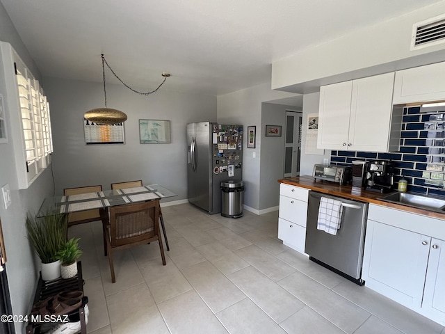 kitchen with butcher block counters, backsplash, stainless steel appliances, white cabinets, and decorative light fixtures