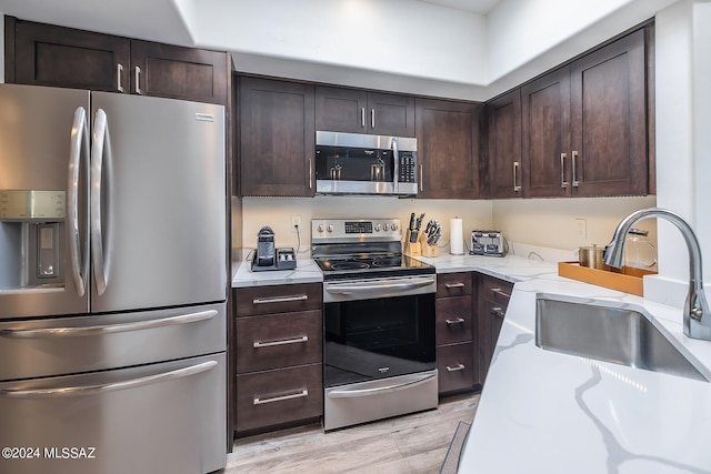 kitchen featuring stainless steel appliances, light wood-type flooring, dark brown cabinets, and sink