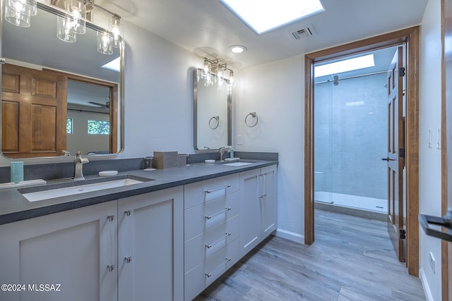 bathroom featuring a skylight, dual vanity, tiled shower, and hardwood / wood-style floors