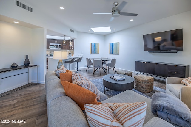 living room with a skylight, dark hardwood / wood-style floors, and ceiling fan