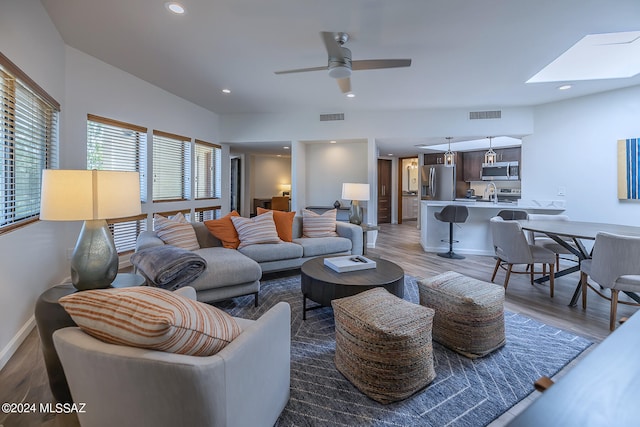 living room with sink, ceiling fan, wood-type flooring, and a skylight