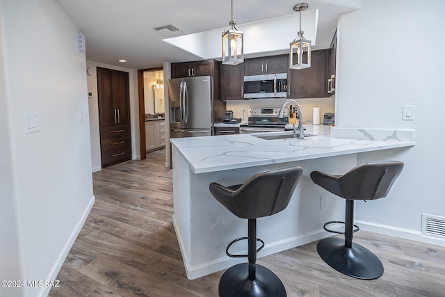 kitchen featuring stainless steel appliances, sink, light stone counters, dark brown cabinetry, and light wood-type flooring