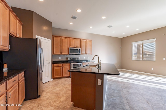 kitchen featuring an island with sink, appliances with stainless steel finishes, dark stone countertops, light tile patterned flooring, and sink