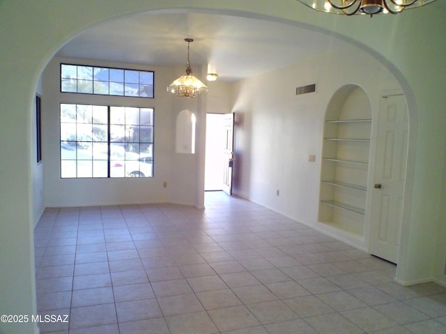 tiled empty room with built in features and a notable chandelier