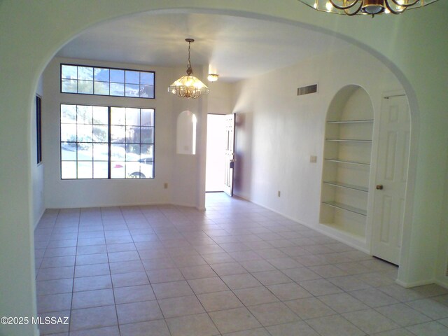 empty room featuring a notable chandelier, built in shelves, and light tile patterned floors