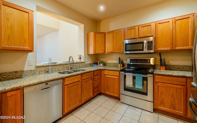 kitchen with appliances with stainless steel finishes, light tile patterned flooring, light stone countertops, and sink