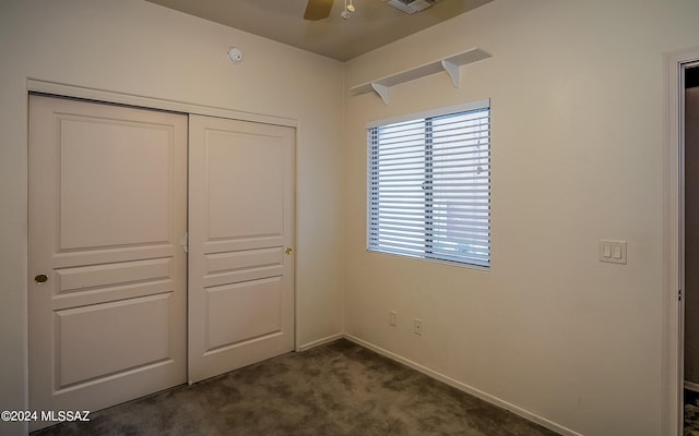 unfurnished bedroom with ceiling fan, dark carpet, and a closet