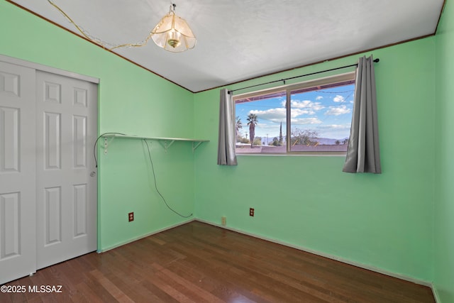 empty room featuring wood finished floors, baseboards, and vaulted ceiling
