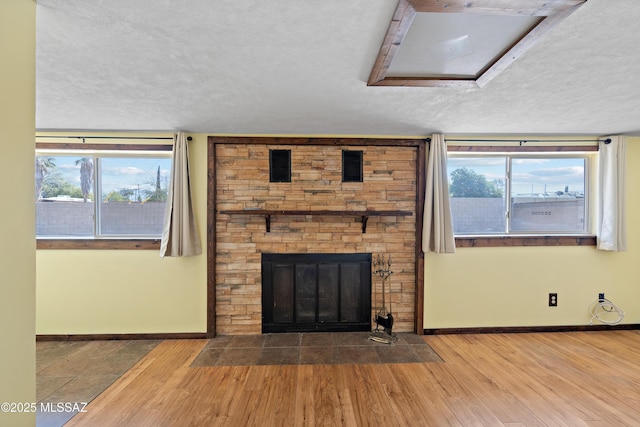 unfurnished living room featuring a textured ceiling, wood finished floors, a fireplace, and baseboards