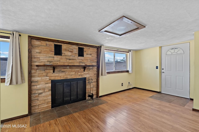 unfurnished living room with a textured ceiling, a stone fireplace, wood finished floors, baseboards, and plenty of natural light