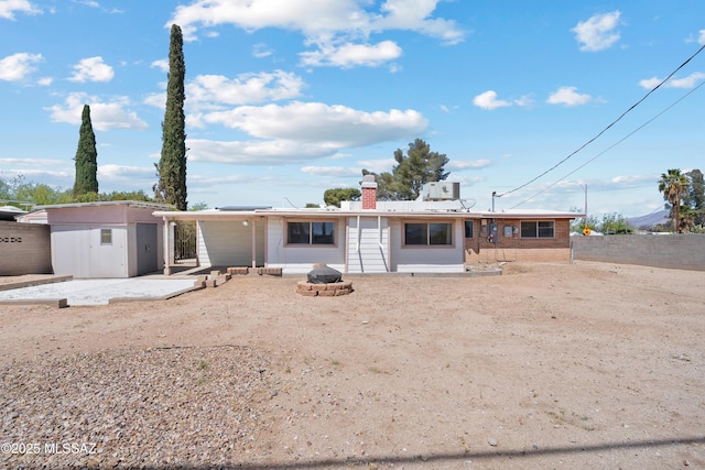 rear view of property with an outdoor structure, an outdoor fire pit, a storage unit, fence, and a chimney