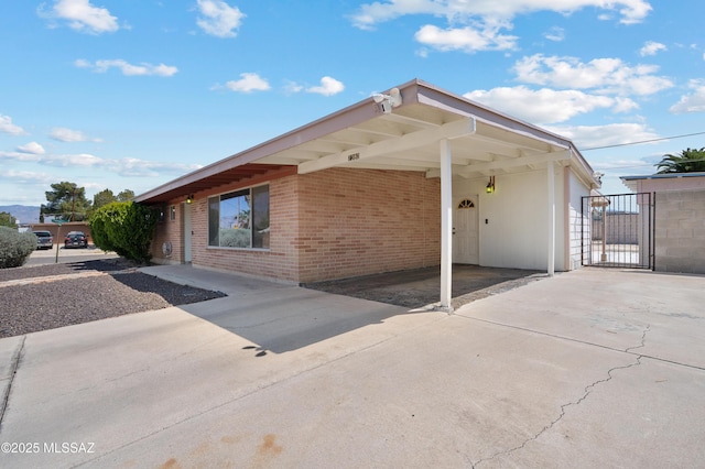 view of side of property featuring a carport, driveway, a gate, and brick siding