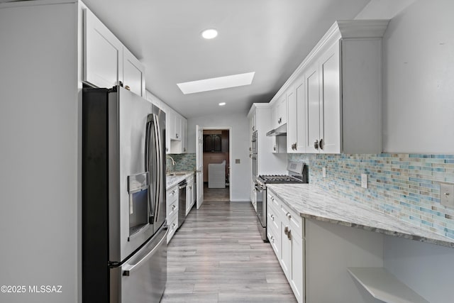 kitchen with recessed lighting, under cabinet range hood, a skylight, stainless steel appliances, and a sink