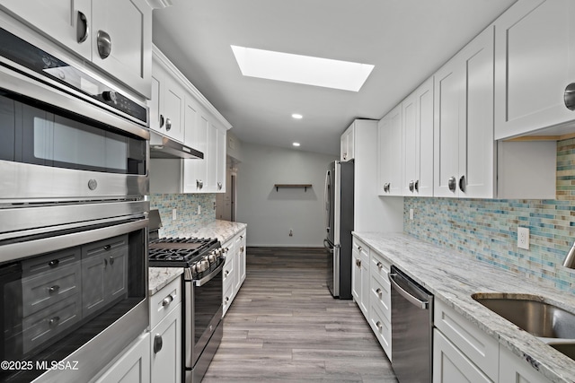 kitchen with white cabinets, a skylight, appliances with stainless steel finishes, a sink, and backsplash