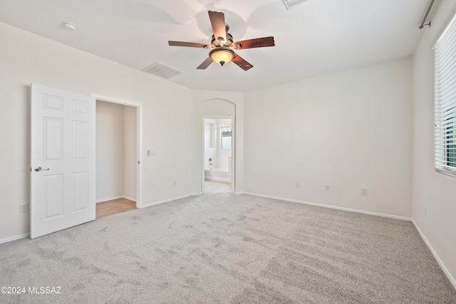 unfurnished bedroom featuring light colored carpet, ensuite bath, and ceiling fan