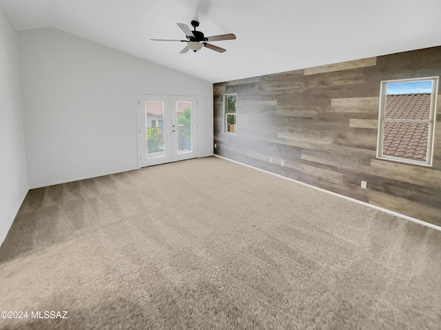 carpeted spare room with french doors, ceiling fan, vaulted ceiling, and wood walls