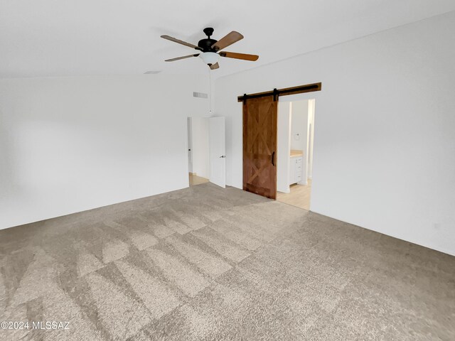 interior space featuring light carpet, a barn door, ensuite bath, and ceiling fan