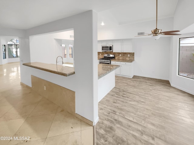 kitchen with appliances with stainless steel finishes, white cabinetry, backsplash, light stone countertops, and light hardwood / wood-style flooring