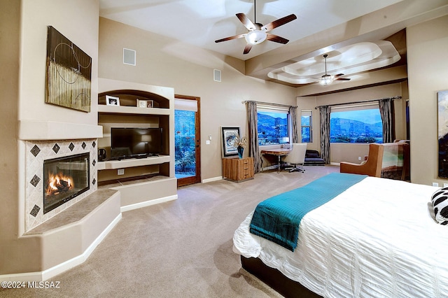 carpeted bedroom featuring ceiling fan, a tray ceiling, and a tile fireplace